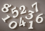 Números brancos espalhados sobre uma superfície neutra, representando contagem, cálculos ou conceitos matemáticos.