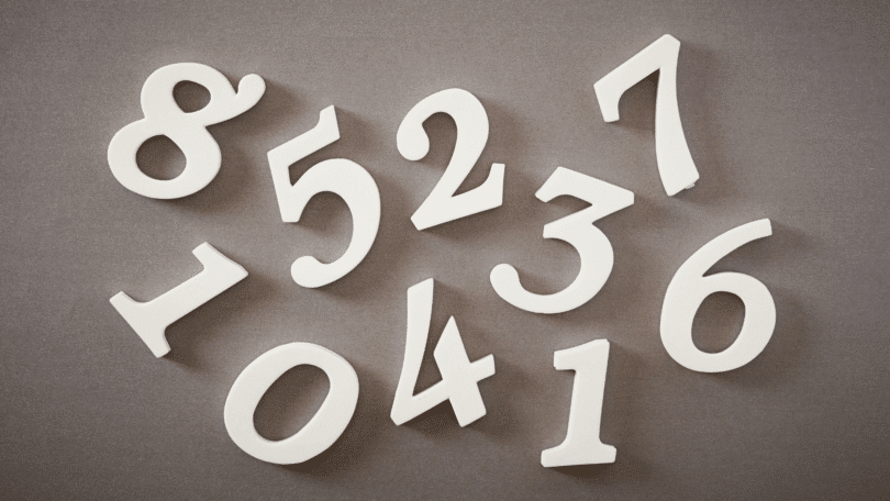 Números brancos espalhados sobre uma superfície neutra, representando contagem, cálculos ou conceitos matemáticos.