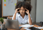 Mulher concentrada diante do notebook, segurando as têmporas em sinal de estresse e sobrecarga mental no trabalho.