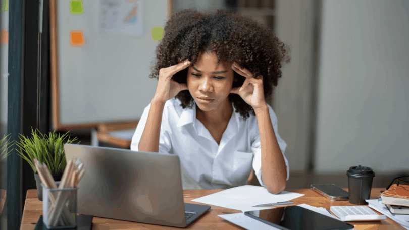 Mulher concentrada diante do notebook, segurando as têmporas em sinal de estresse e sobrecarga mental no trabalho.