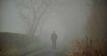 Imagem de uma figura humana caminhando por uma estrada envolto em névoa suave, com raios de luz atravessando o cenário.
