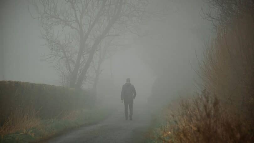 Imagem de uma figura humana caminhando por uma estrada envolto em névoa suave, com raios de luz atravessando o cenário.