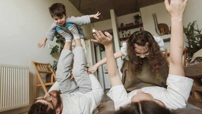 Imagem de um casal bricando com seus filhos dentro de uma sala de estar, simbolizando a relação de momentos simples e as memórias que eles guardam para a vida.