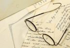 Óculos antigos sobre cartas manuscritas e envelopes espalhados em uma superfície clara.