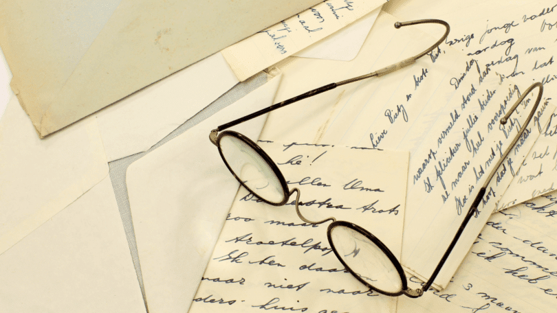 Óculos antigos sobre cartas manuscritas e envelopes espalhados em uma superfície clara.