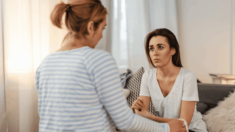 Duas pessoas conversam em ambiente interno, com expressão de preocupação e apoio emocional.