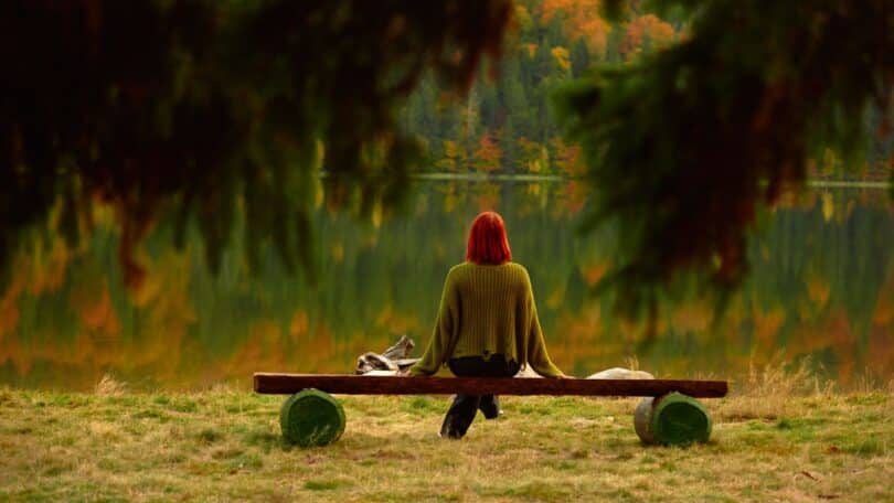 Imagem de uma pessoa sentada em um banco diante de um lago ao amanhecer, natureza tranquila, atmosfera contemplativa, luz suave, sensação de paz.