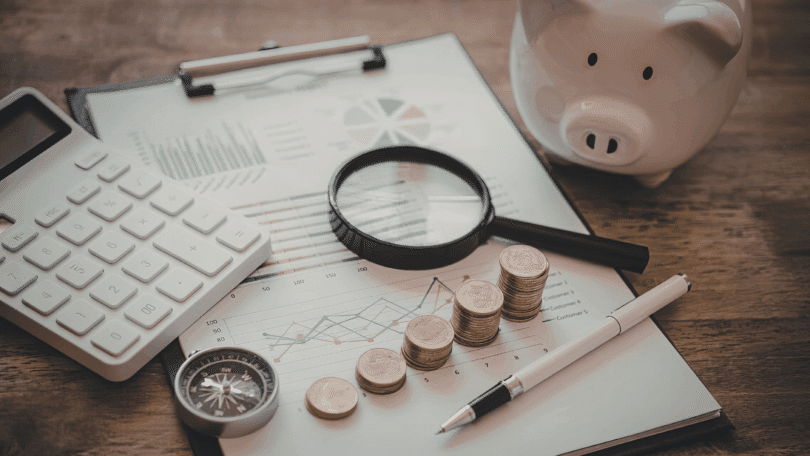 Calculadora, moedas, cofrinho e gráficos financeiros sobre a mesa, simbolizando planejamento e economia.