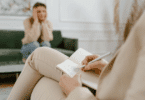 Profissional faz anotações enquanto conversa com uma pessoa em atendimento psicológico ou terapêutico.