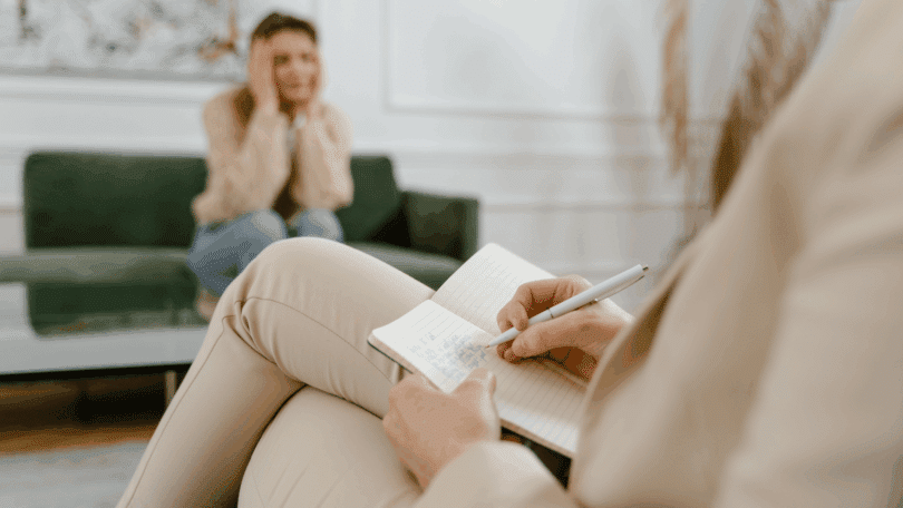 Profissional faz anotações enquanto conversa com uma pessoa em atendimento psicológico ou terapêutico.