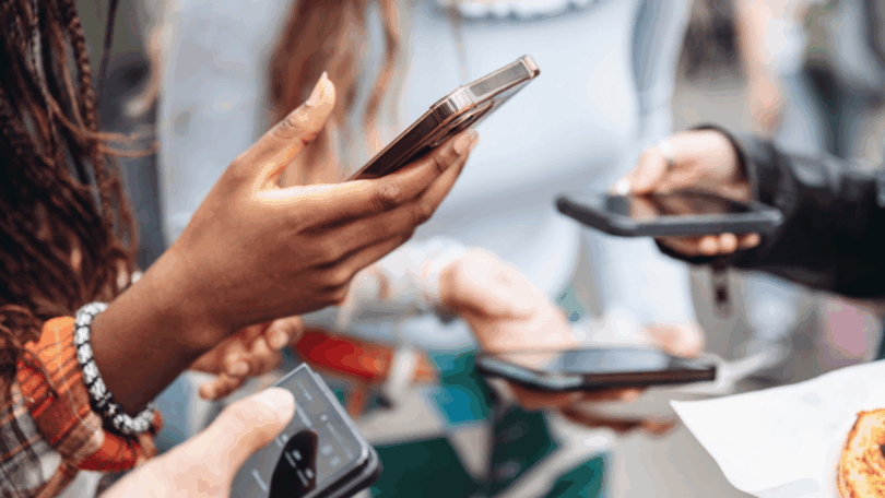 Pessoas seguram smartphones nas mãos, representando uso compartilhado de tecnologia e comunicação digital.