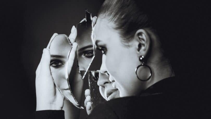 Imagem de uma mulher refletindo olhando no espelho, buscando o autoconhecimento.