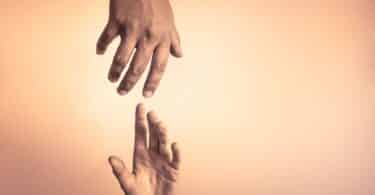 Imagem de duas mãos se encontrando, ajudando outra a se levantar, em um cenário iluminado e acolhedor, trazendo um conceito de esperança, caridade, empatia e amor ao próximo.