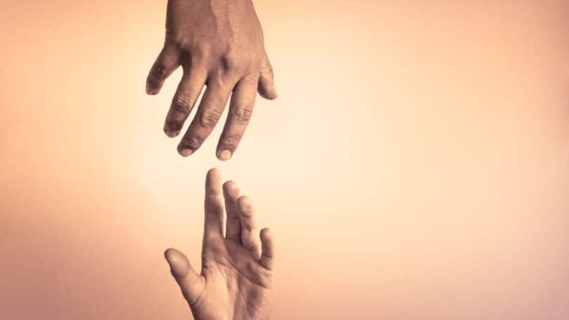 Imagem de duas mãos se encontrando, ajudando outra a se levantar, em um cenário iluminado e acolhedor, trazendo um conceito de esperança, caridade, empatia e amor ao próximo.