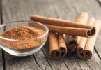 Tigela de canela em pó ao lado de vários paus de canela sobre uma mesa de madeira.
