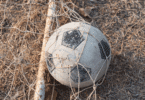 Bola de futebol desgastada presa em uma rede sobre a grama seca.
