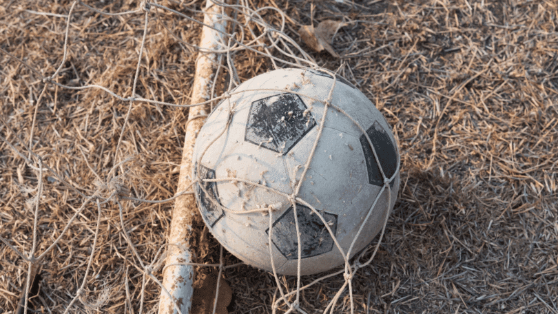 Bola de futebol desgastada presa em uma rede sobre a grama seca.