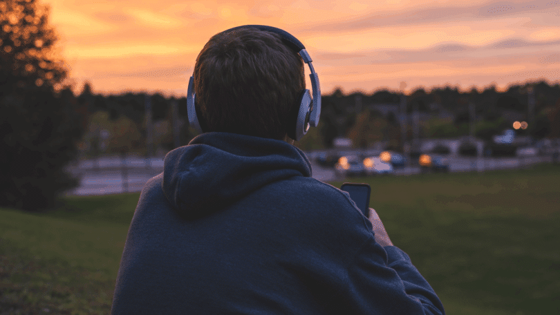 Homem de fones de ouvido observa o pôr do sol enquanto segura um celular.