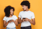 Casal olha para os celulares, aparentando surpresa durante uma conversa.