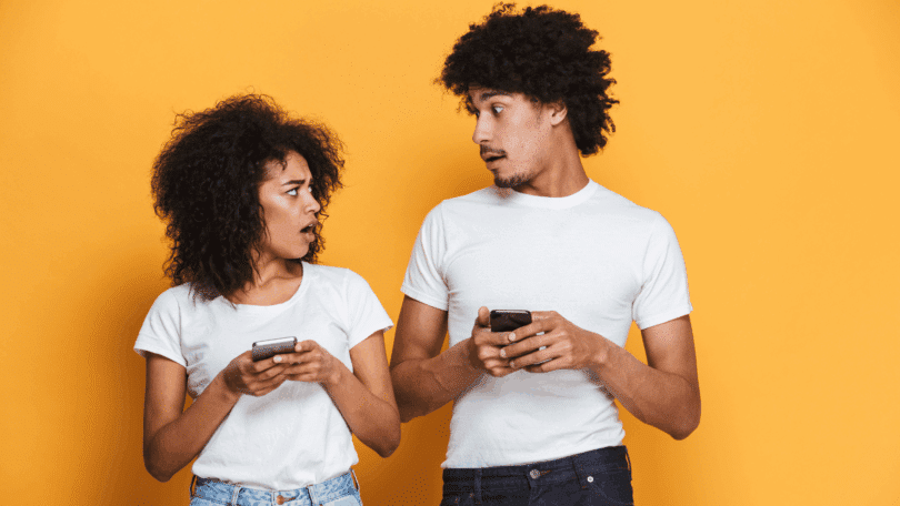 Casal olha para os celulares, aparentando surpresa durante uma conversa.