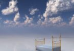 Imagem do céu com nuvens brancas e em destaque uma cama de ferro dourado e lençol branco, simbolizando o sono e os sonhos.