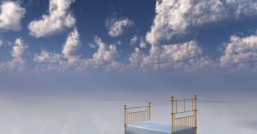 Imagem do céu com nuvens brancas e em destaque uma cama de ferro dourado e lençol branco, simbolizando o sono e os sonhos.
