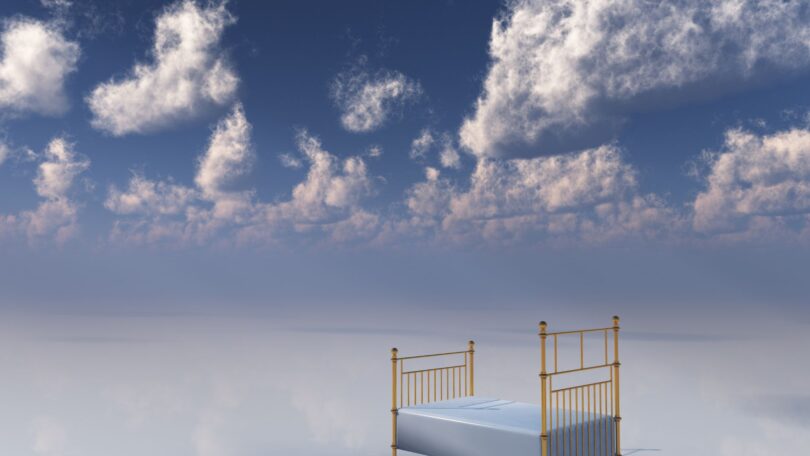Imagem do céu com nuvens brancas e em destaque uma cama de ferro dourado e lençol branco, simbolizando o sono e os sonhos.