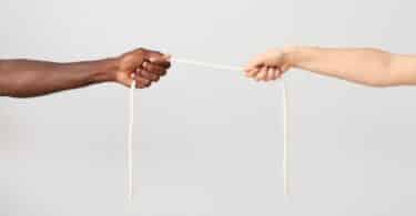Imagem de dois braços, um de uma pessoa negra e outro de uma pessoa branca, segurando uma corda esticada entre eles, simbolizando a xenofobia, o preconceito e a divisão entre pessoas de diferentes origens.