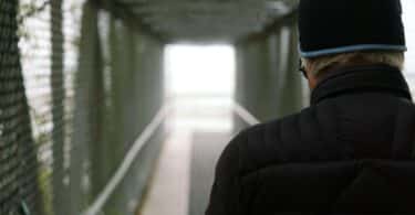 Imagem de um homem usando um gorro de lã e uma roupa de frio na cor preta, tentando atravessar uma ponte, porém ele tem gefirofobia.