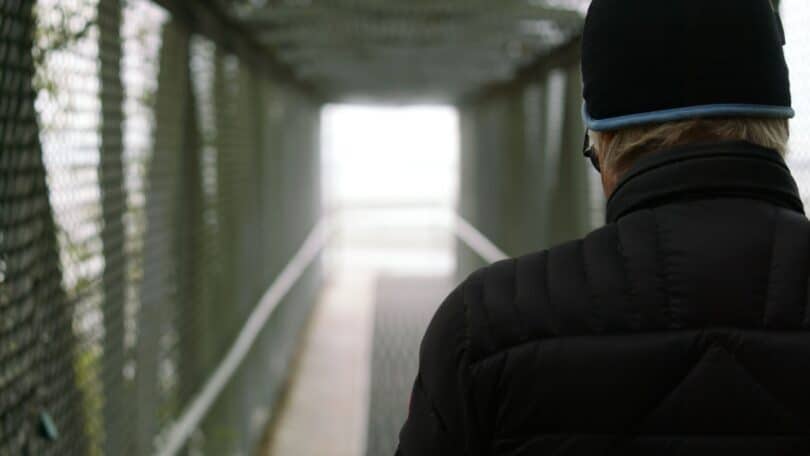 Imagem de um homem usando um gorro de lã e uma roupa de frio na cor preta, tentando atravessar uma ponte, porém ele tem gefirofobia.