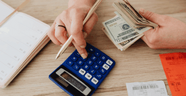 Pessoa calculando despesas e organizando as finanças com dinheiro em dólares, calculadora, agenda e recibos sobre uma mesa.