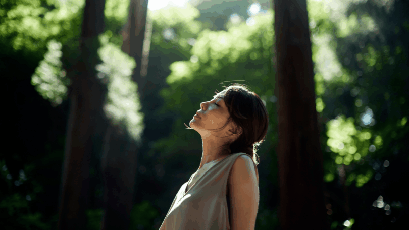 Mulher de olhos fechados respira profundamente em meio à natureza, aproveitando um momento de paz e conexão interior.