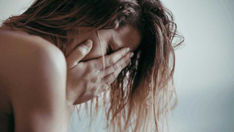 Mulher cobre o rosto com as mãos, expressando tristeza, angústia e sofrimento emocional.