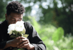Homem segurando um buquê de rosas brancas, de olhos fechados, em um momento de reflexão e contemplação na natureza.