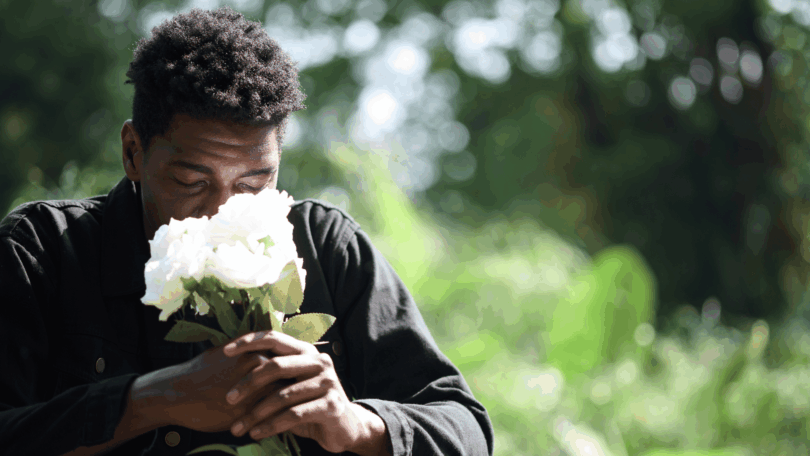 Homem segurando um buquê de rosas brancas, de olhos fechados, em um momento de reflexão e contemplação na natureza.