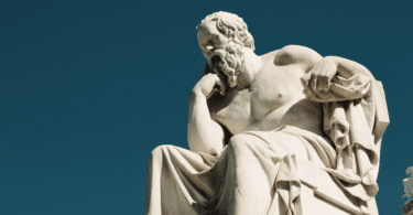 Escultura de mármore de Sócrates sentado, com a mão apoiada no rosto em uma pose reflexiva, sob um céu azul.
