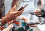 Pessoas seguram celulares durante uma interação em grupo, destacando o uso da tecnologia no cotidiano.