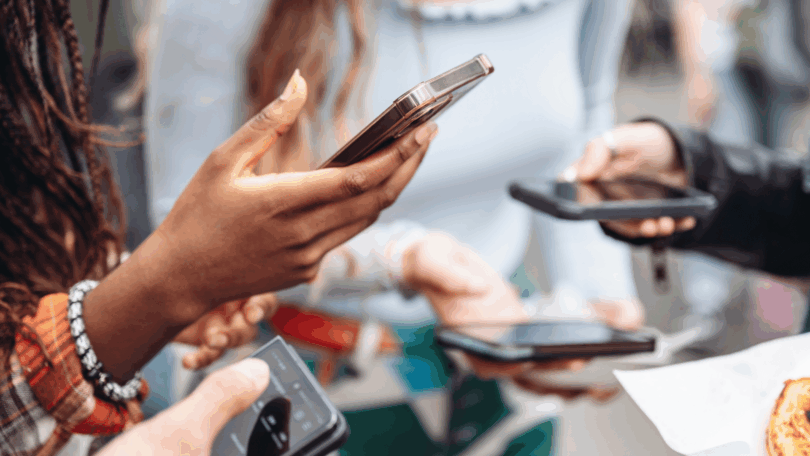 Pessoas seguram celulares durante uma interação em grupo, destacando o uso da tecnologia no cotidiano.