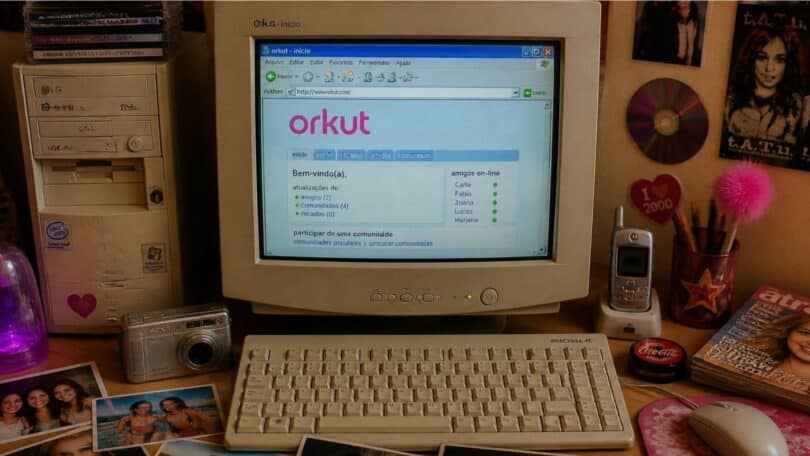 Imagem de um computador antigo com a tela da página inicial do orkut, teclado, fotografias impressas e objetos que remetam ao início dos anos 2000.